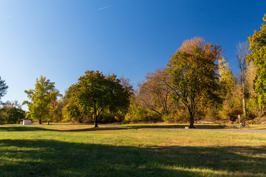 View of the autumn landscape at Valley Forge National Historical Park with vibrant fall foliage on the trees, a clear blue sky, and a grassy field in Valley Forge, Pennsylvania, United States.