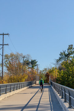 View of a cyclist riding on a paved path surrounded by autumn trees and metal railings in Valley Forge, Pennsylvania, United States.