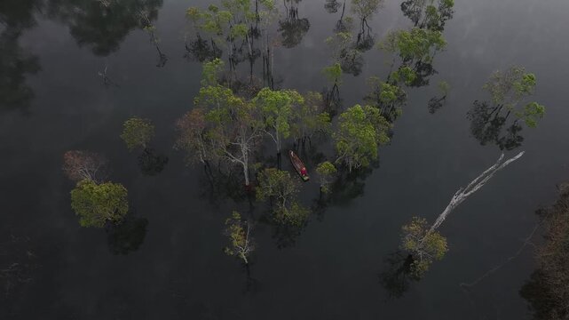 Aerial drone view of a fisherman rowing across Tuyen Lam Lake at sunrise near Suoi Tia in Xuan Huong, Da Lat, Vietnam, surrounded by peaceful pine forests.