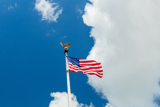 View of the American flag waving on a flagpole with an eagle finial against a blue sky with white clouds at Valley Forge, Pennsylvania, United States.