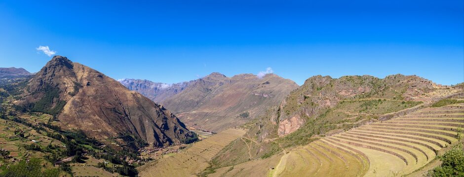 View of the ancient Inca agricultural terraces at the Pisac archaeological site, set against rugged Andean mountains under a clear blue sky in Pisac, Cusco, Peru.