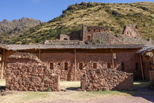 View of the ancient stone ruins of Pisac with traditional masonry walls and thatched roof structures set against a rugged mountain landscape in Pisac, Cusco, Peru.