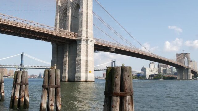Brooklyn Bridge and Manhattan Bridge from Downtown, New York City, United States. Esplanade park. American architecture, famous tourist landmark. Waterfront urban promenade. Old wooden pier piles.