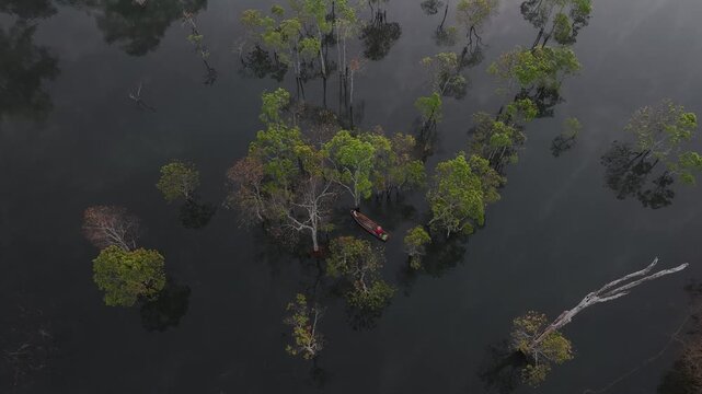 Aerial drone view of a fisherman rowing across Tuyen Lam Lake at sunrise near Suoi Tia in Xuan Huong, Da Lat, Vietnam, surrounded by peaceful pine forests.