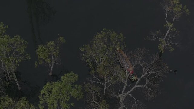 Aerial drone view of a fisherman rowing across Tuyen Lam Lake at sunrise near Suoi Tia in Xuan Huong, Da Lat, Vietnam, surrounded by peaceful pine forests.