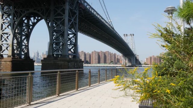 Williamsburg Bridge in Brooklyn, New York City, United States. Transport metallic bridge over East River water near Marcy Av subway station and Domino park in Williamsburg. Riverfront summer promenade