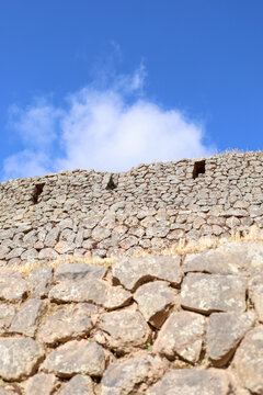 View of the ancient Inca stone walls of the Pisac archaeological site under a clear blue sky in Pisac, Cusco, Peru.