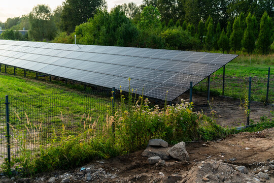 View of solar panels installed in a grassy field with trees in the background and a wire fence in Dabrowa Gornicza, Silesian Voivodeship, Poland.