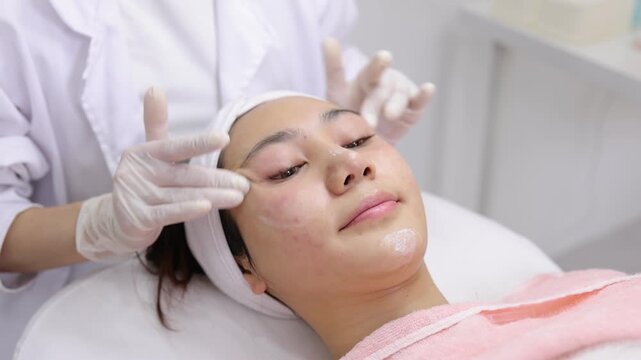 Professional cosmetologist massaging a woman's face with moisturizing cream. Relaxing anti-aging skin care procedure in a wellness clinic.