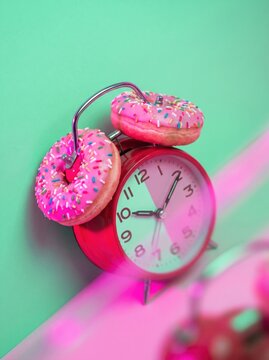 Red alarm clock with pink frosted donuts as bells on green background, creative concept with colorful sprinkles and playful mood