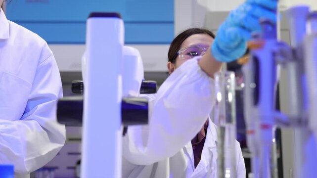Female scientist working in a laboratory conducting an experiment. Asian female scientist wearing a lab coat and protective glasses carefully performing a chemical experiment in a high-tech laboratory