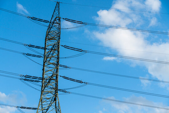 View of a tall metal electricity pylon with power lines stretching across a bright blue sky with light clouds in Dabrowa Gornicza, Silesian Voivodeship, Poland.