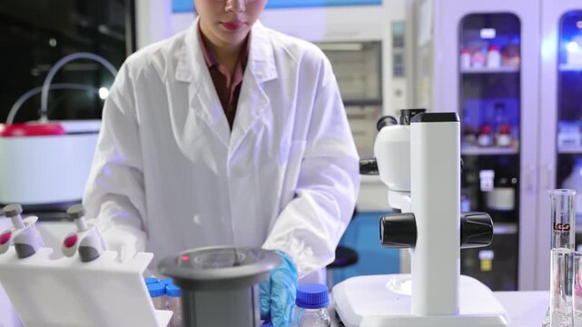Female scientist using a microscope in a laboratory. Young Asian scientist conducting experiment, using microscope and handling test tubes. Medical or pharmaceutical research in lab.