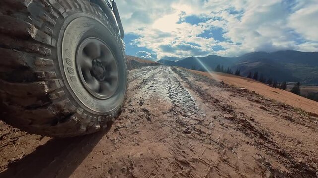 Heavy off road vehicle tire driving across a wet and muddy mountain track, Rugged terrain and distant mountain peaks create an adventurous travel scene