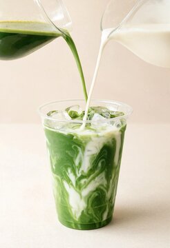 Fresh green matcha tea being poured with milk into a plastic cup with ice cubes