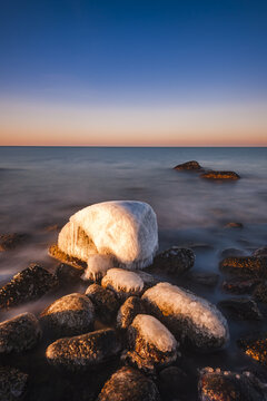View of ice-covered rocks along the shoreline at Nasbokrok during golden hour with calm sea and clear sky in Asa, Hallands lan, Sweden.