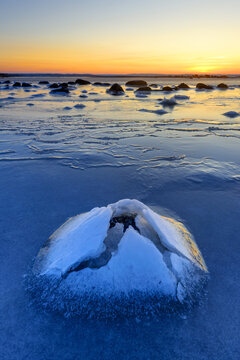 View of the frozen sea at Nasbokrok with a unique ice formation in the foreground under a vibrant sunset sky in Asa, Hallands lan, Sweden.