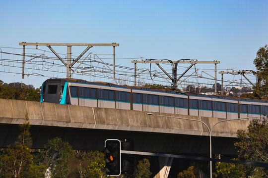 View of a driverless metro train traveling on elevated railway infrastructure through a suburban landscape under a clear blue sky in Sydney, New South Wales, Australia.