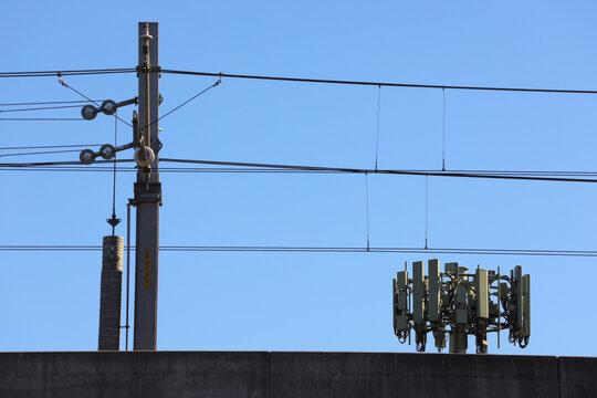 View of a 5G telecommunications tower with cellular antenna arrays behind elevated metro rail infrastructure and overhead electrical lines in Sydney, New South Wales, Australia.