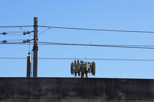 View of a cellular antenna array mounted on a concrete wall with overhead electrical power lines against a clear blue sky in Sydney, New South Wales, Australia.