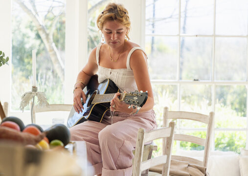 stylish young woman playing guitar in light filled room