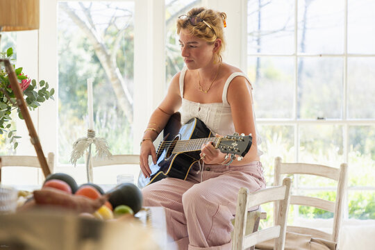 stylish young woman playing guitar in light filled room