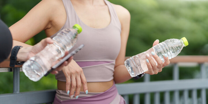 Cropped shot of women holding water bottles and smartphone for hydration and workout