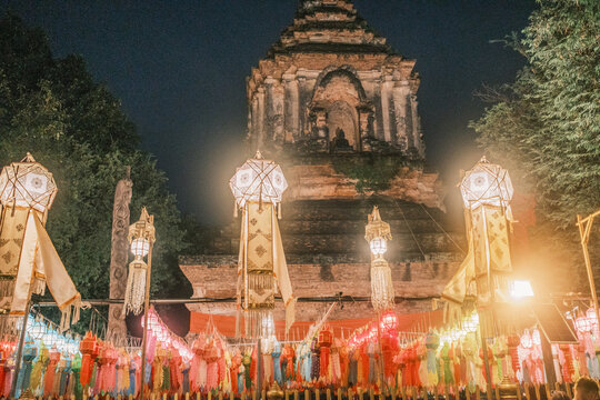 View of the ancient brick chedi at Wat Lok Moli illuminated by colorful traditional Lanna lanterns during the Yi Peng festival in Chiang Mai, Thailand.