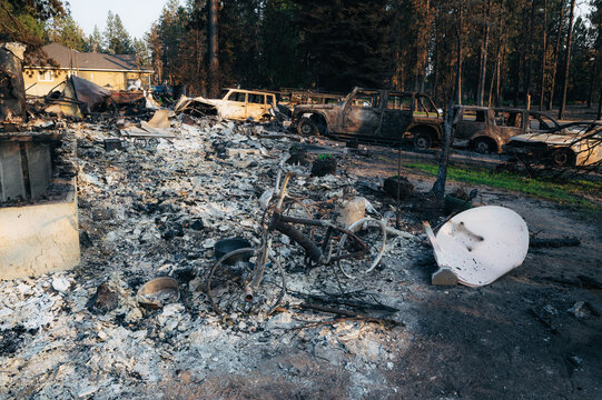View of the aftermath of a wildfire, featuring charred vehicles, debris, and a bicycle amidst the ash in Spokane, Washington, United States.