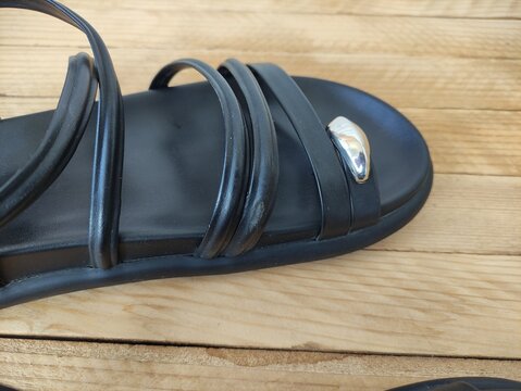 Close up of black sandal straps with silver metal ornament on wooden surface