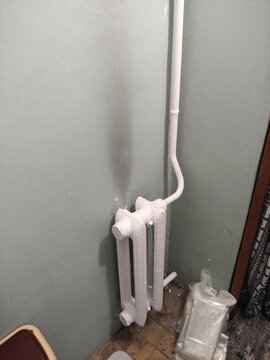 Small white cast iron radiator with white pipe on green painted wall in corner