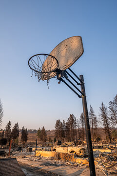 View of a damaged basketball hoop standing in a landscape devastated by wildfires, with scorched trees and debris visible in the background in Spokane, Washington, United States.