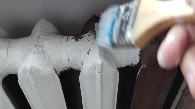 Person holding a paint brush and painting a cast iron radiator white, first person view video