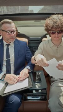 Vertical video of middle aged Caucasian businessman and young partner discussing documents in car, with young man tearing up papers. Ideal for corporate conflict concepts