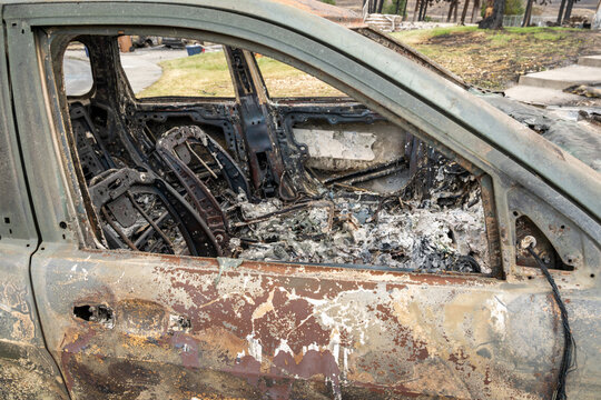 View of a car completely destroyed by fire with charred interior and ash-covered metal frame in the aftermath of a wildfire in Spokane, Washington, United States.