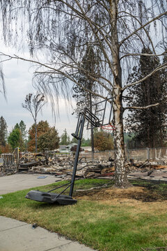 View of a basketball hoop standing in front of the charred ruins of a residential home destroyed by wildfire in Spokane, Washington, United States.