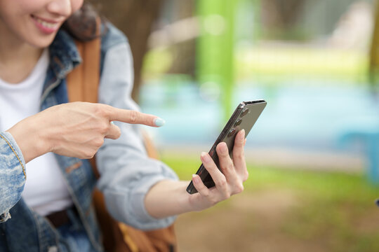 Asian female tourist pointing at smartphone screen outdoors for travel navigation