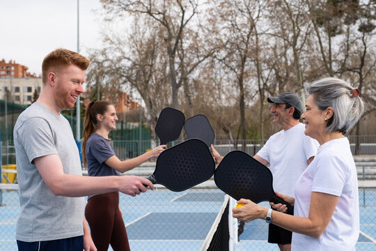 Group of friends socializing and laughing while playing pickleball outdoors