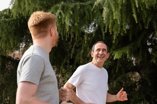 Two men jogging outdoors, smiling and happy while exercising for health and wellness