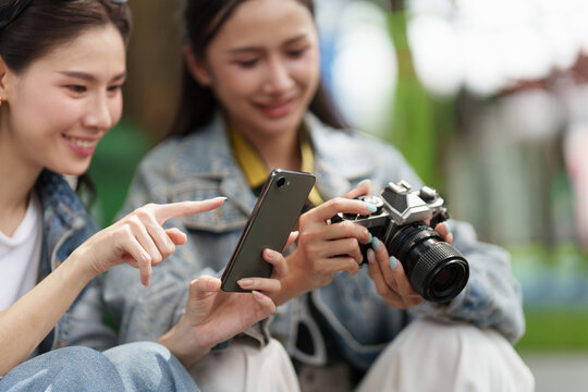 Asian women travelers checking smartphone photos and camera during vacation trip outdoors