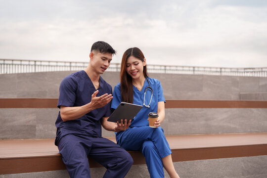 Asian healthcare workers discussing digital tablet outdoors during breaktime