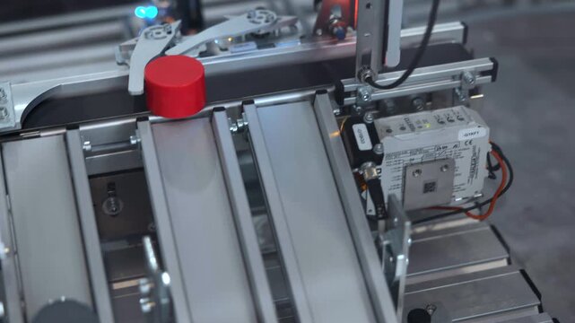 Close top-down industrial automation machinery with parallel metal conveyor rails, red and black cylindrical components, compact control modules, and cool factory lighting