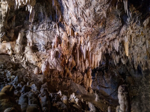 Majestic limestone cavern interior featuring intricate dangling stalactites and sturdy stone stalagmites illuminated by soft artificial lighting within this ancient deep natural subterranean rock 