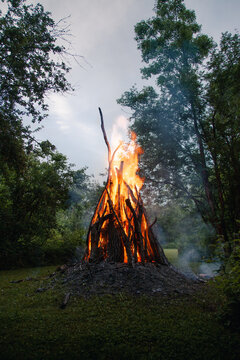 View of a large bonfire burning in a wooded area on Vormsi island, with bright flames rising from stacked branches and logs in Laane County, Estonia.