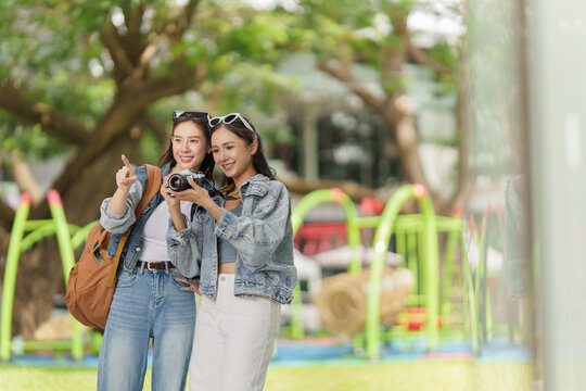 Asian female tourists holding camera and pointing into distance for travel sightseeing