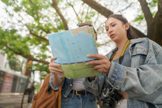 Asian female tourists holding map planning route during vacation trip outdoors