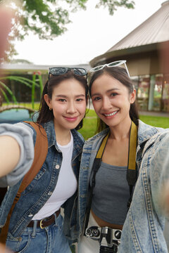 Asian women tourists taking selfie while enjoying vacation trip in outdoor park
