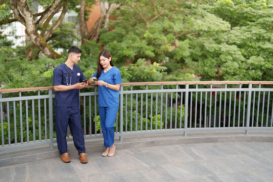 Asian male and female nurses using smartphones on balcony during breaktime