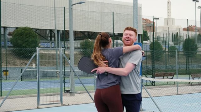 Happy man and woman high fiving and hugging after scoring a point on a pickleball court