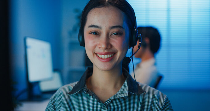 Gen z Asia young call center team or customer support service executive use computer and microphone headset work smile and looking at camera in late night office. Telemarketing or sales job concept.